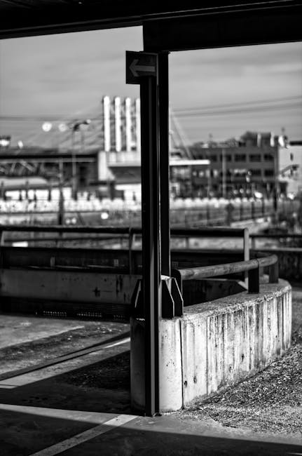 A black and white photo of an abandoned urban railway station with concrete structures and a distant view of a cityscape.
